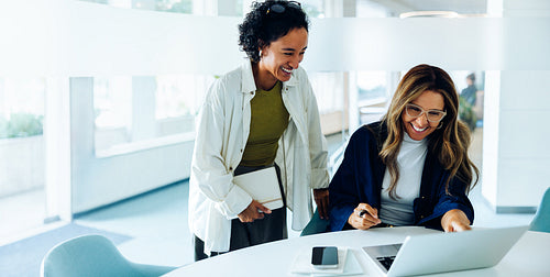 Two women work together at a laptop in office