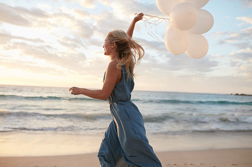 Beautiful woman running on the beach with balloons