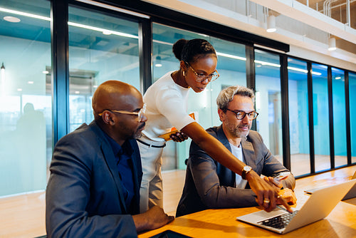 Three professionals discussing a project while using a laptop in a meeting