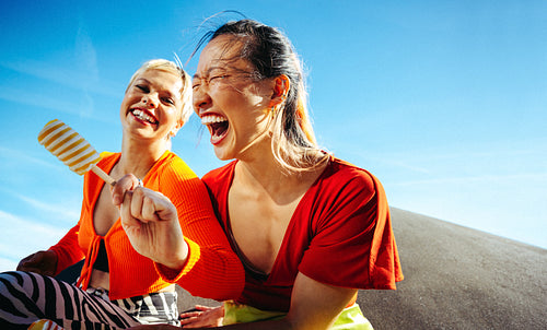 Young women enjoy popsicles and laughter under the summer sky