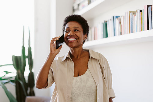 Mature black woman in a living room, smiling and speaking on a mobile phone
