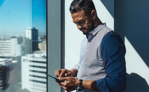 Business investor using phone standing near a window in office.