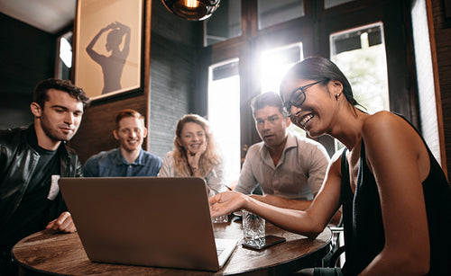 Smiling woman showing something on laptop to her friends