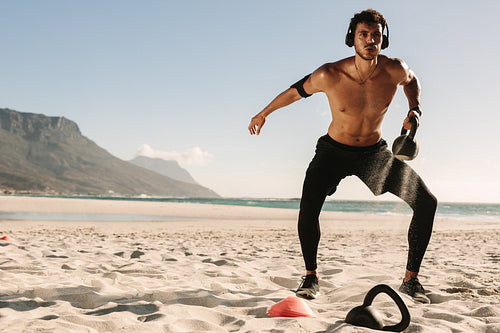 Man doing fitness training at the beach with kettlebells