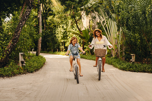 Happy mother and daughter biking at tropical resort island enjoying a sunny day