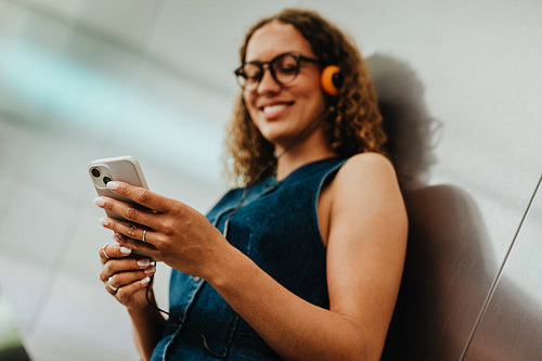 Young woman smiles at smartphone during urban commute with headphones