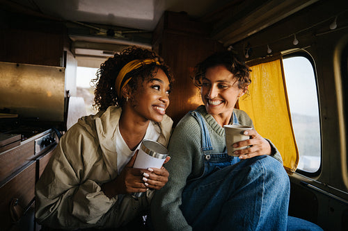 Two friends share coffee and laugh inside a cozy van during travel