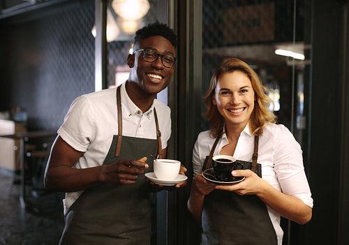 Café owners at their coffee shop holding coffee cups
