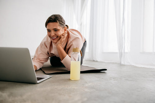 Woman using laptop on yoga mat for online fitness session at home