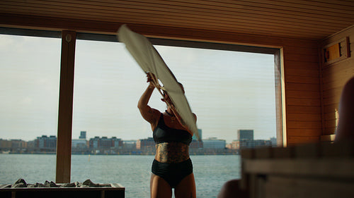 Woman leads a sauna ritual with aufguss and fan work in a wooden spa
