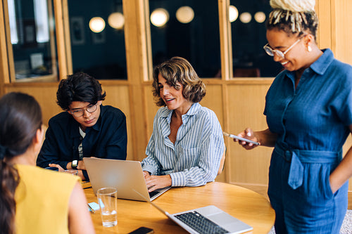 Four coworkers collaborating around a desk with laptops and smartphones