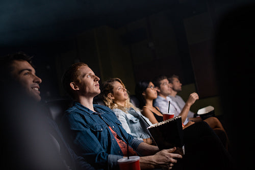 Young man with friends in cinema hall watching movie
