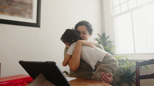 Motherly love and support during e-learning: Mom hugging and kissing her son in a homeschooling session