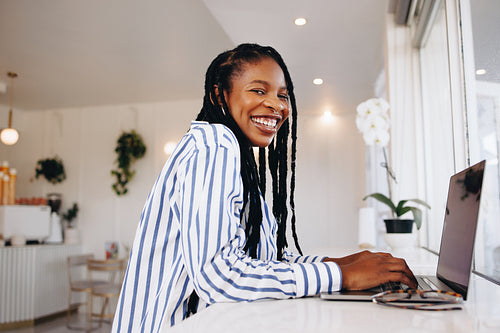 Happy female freelancer smiling at the camera while working on a laptop in a coffee shop