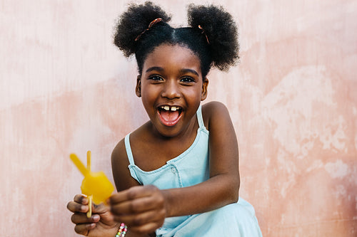 Cheerful afro girl enjoying frozen fruit popsiclse at home