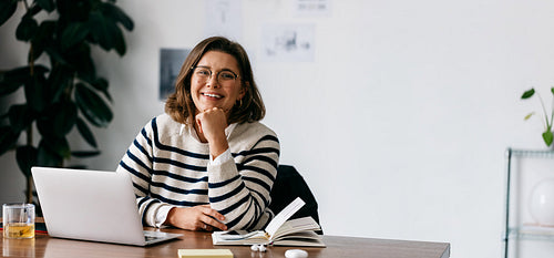 Professional woman smiling at desk with laptop and notebook