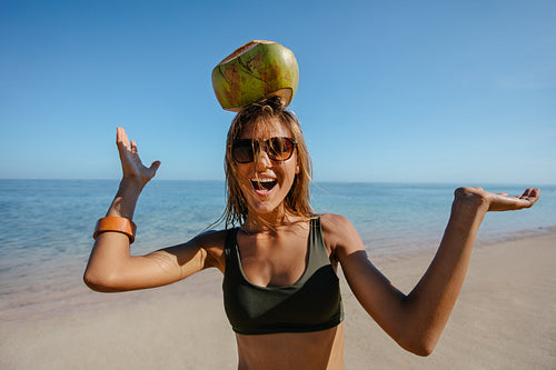 Happy woman balancing a coconut on her head at the beach
