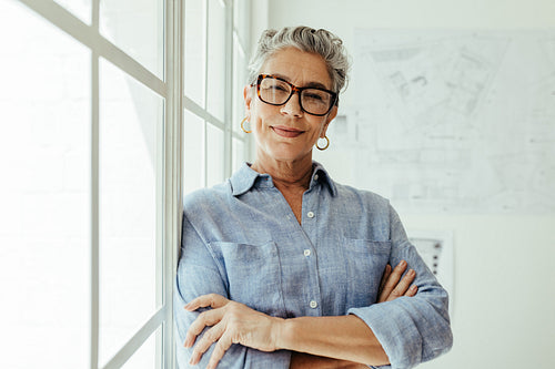 Senior designer with grey hair standing in her office, looking at the camera confidently