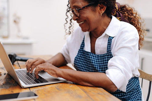 Happy senior business woman using a laptop to manage orders from her clients