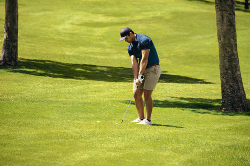 Sportsman preparing for a golf shot on the fairway lining up golf club with the golf ball.