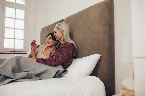 Woman sitting on bed with her old mother