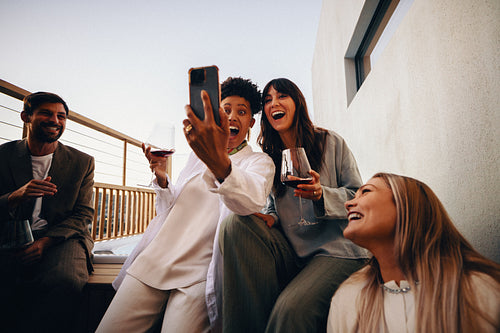 Group of friends enjoying wine and selfies together outdoors on a deck