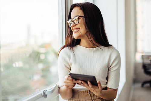 Business woman holding a tablet and standing next to a window