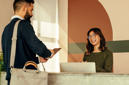 Happy receptionist assisting a man with signing in to an office