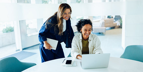 Two women work together at laptop in office