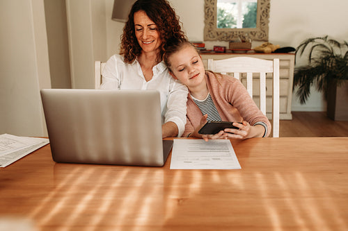 Mother working from home with daughter using smart phone