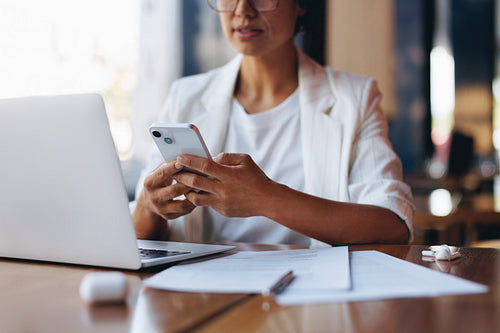 Businesswoman texting on smartphone while working in a cafe with laptop