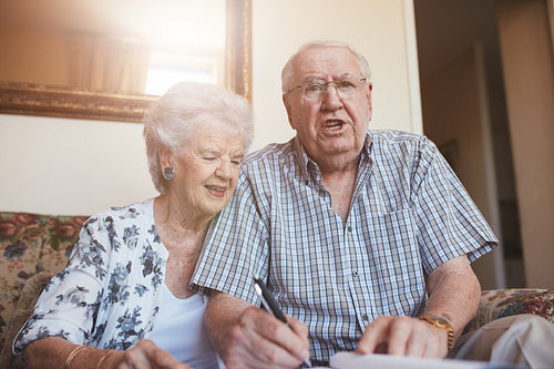Elderly couple signing documents while sitting at home