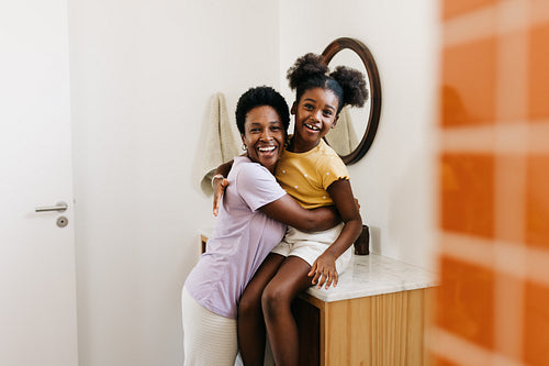 Mother and daughter sharing a morning routine of self-care, smiling together at the bathroom sink