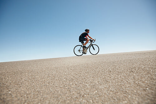 Male cyclist riding on a flat road against blue sky