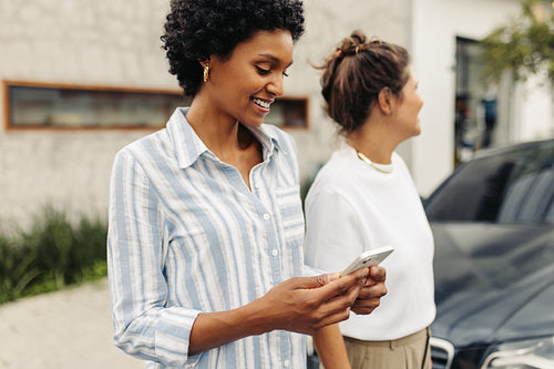 Happy young woman e-hailing a taxi while standing with her friend