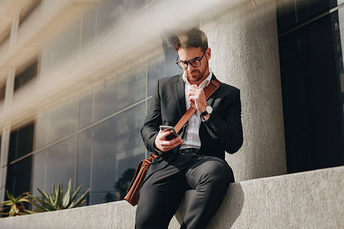 Businessman sitting outdoors checking his mobile phone