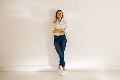 Happy young businesswoman standing against an office wall