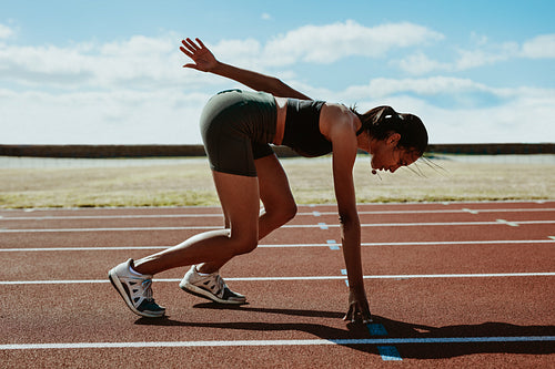 Woman runner at the start line taking position on a running track