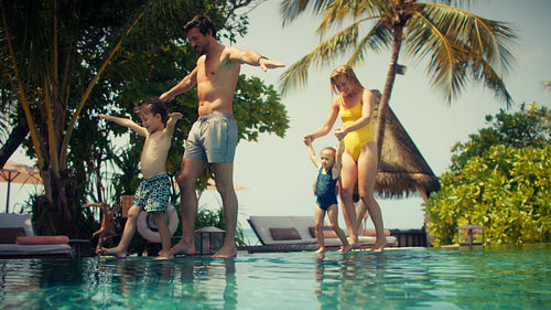 Family enjoys tropical pool vacation, walking carefully along the water's edge