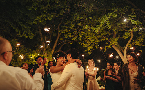 Happy couple dancing surrounded by family under sparklers at night
