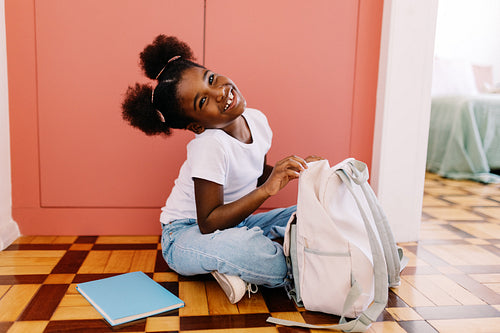 Happy afro girl packing school bag during her morning routine