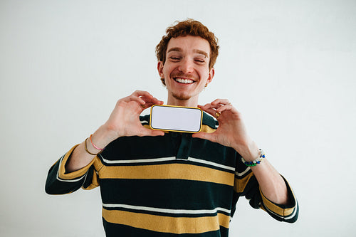 Man holding smartphone in studio portrait with blank screen and friendly smile