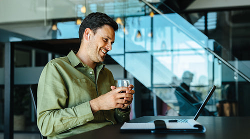 Smiling businessman enjoys an online meeting while having a refreshing drink
