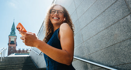 Smiling woman ascends city stairs checking smartphone outdoors