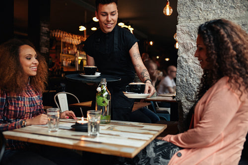 Waiter serving coffee to young women at cafe