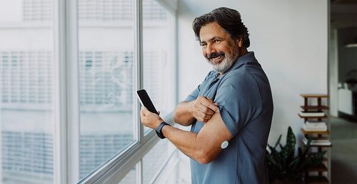 Senior man shows glucose sensor with smartphone at home