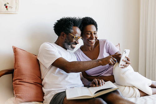Couple relaxing together in bed, engaging with a smartphone