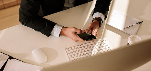 Businessman using mobile phone sitting in front of computer