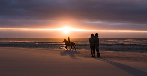 Couple enjoying sunset with woman riding a horse at beach
