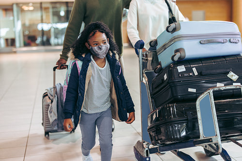 Young girl in face masks walking along parents at airport